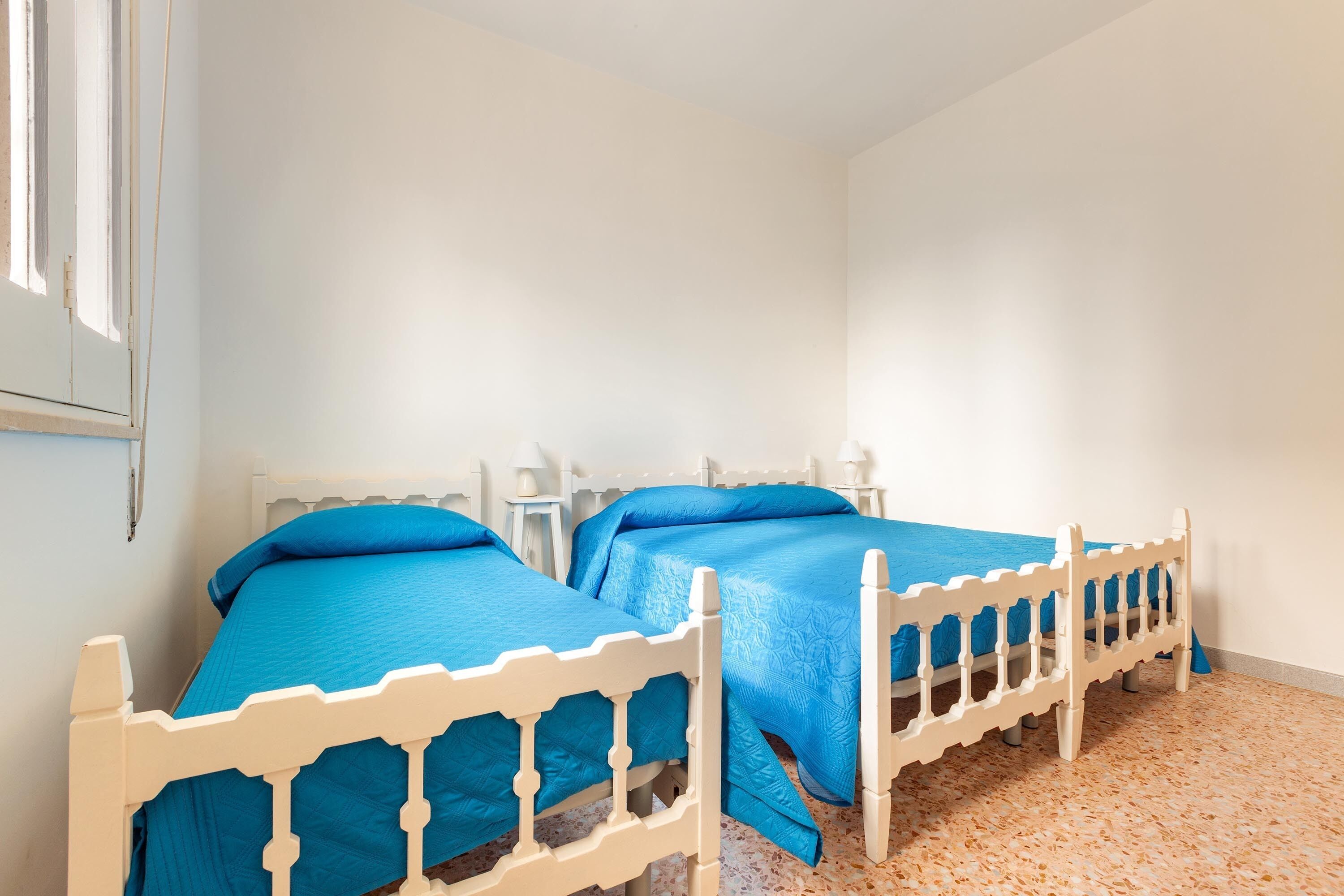 Een slaapkamer met twee bedden, witte hoofdeinden en een betegelde vloer.
