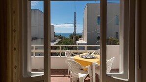 Un balcó amb una taula preparada per dinar, cadires blanques i vista al mar i edificis.