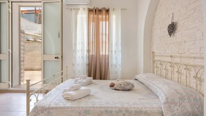 A bedroom with a bed, a wall-mounted light fixture, and a view through an open door.