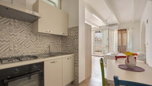 A modern kitchen with a gas stove, oven, and patterned backsplash. There is a dining area with a table, chairs, and a vase with flowers.