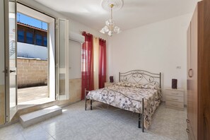 Ein Schlafzimmer mit einem Bett, einem Nachttisch, einer Kommode, einer Deckenleuchte und einer Glastür, die zu einem Außenbereich führt.