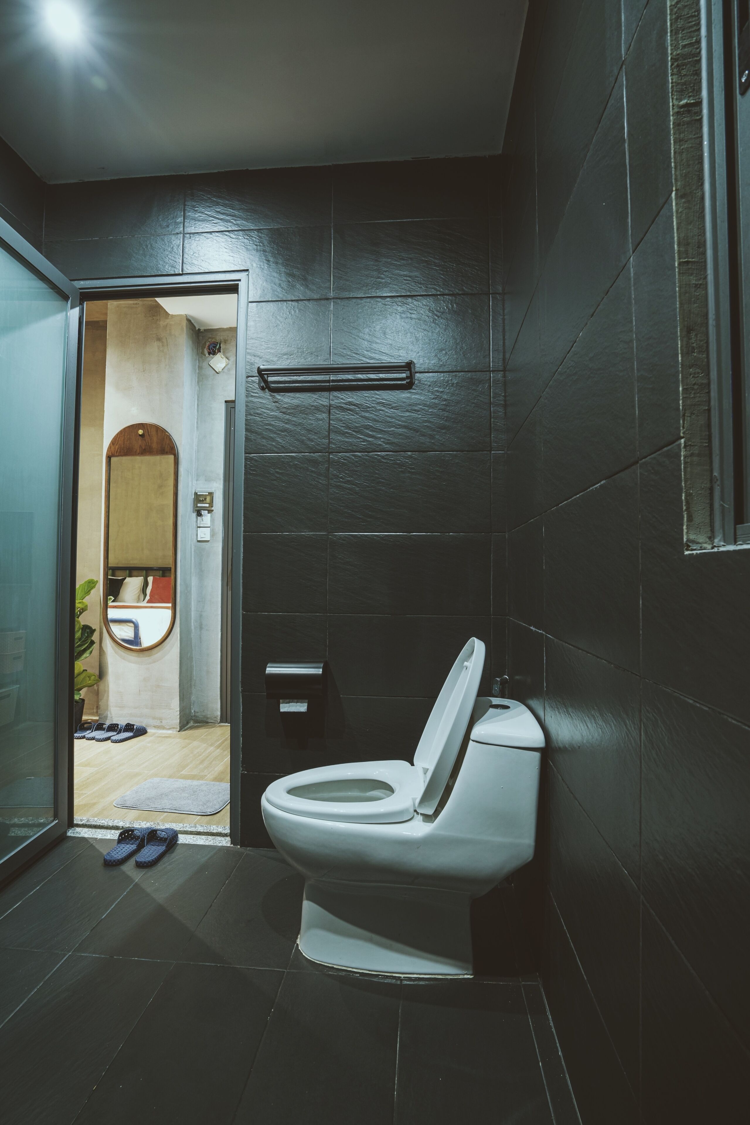 A modern bathroom with dark tiled walls, a white toilet, and a glass shower enclosure.