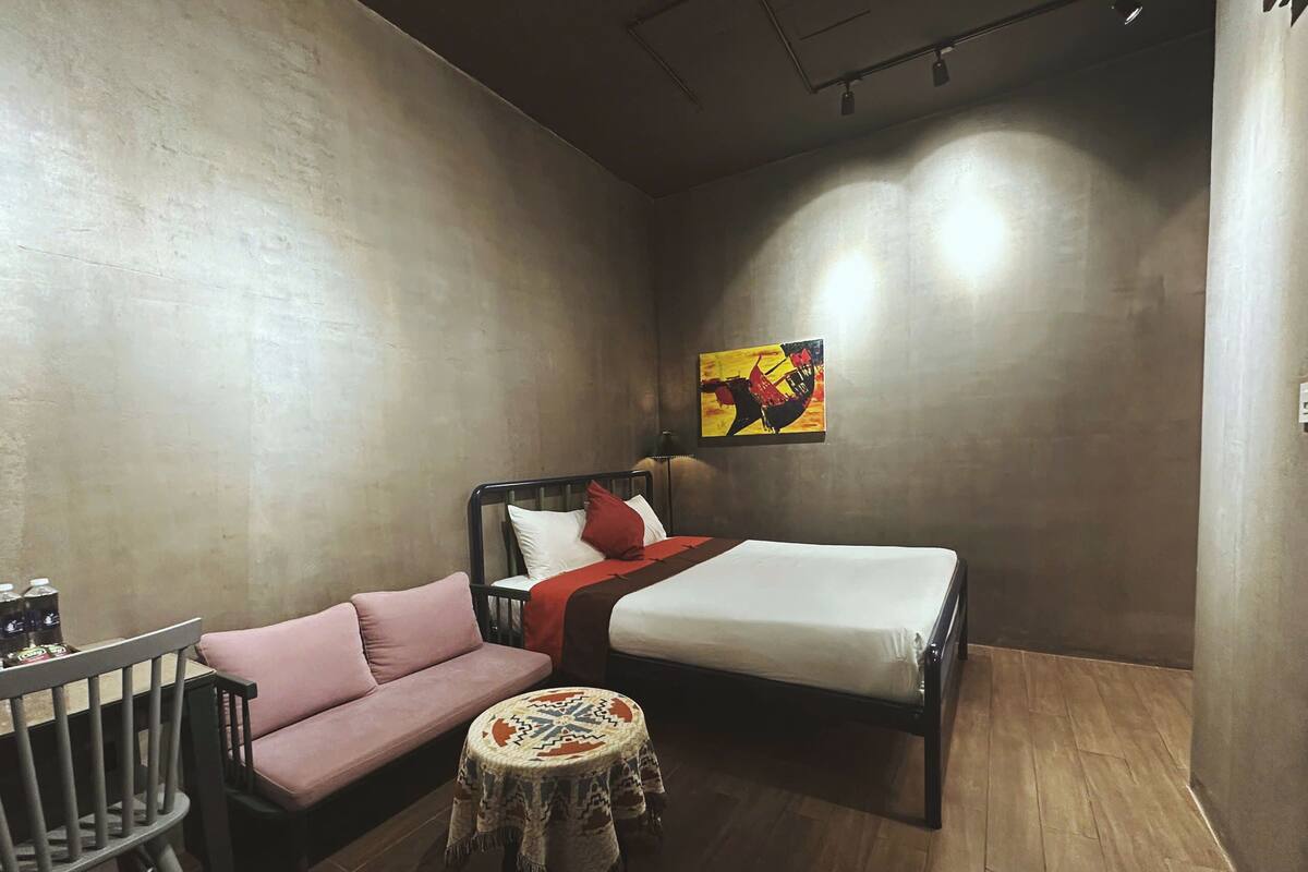 A small, cozy room with a bed, a sofa, a round table, and a painting on the wall.