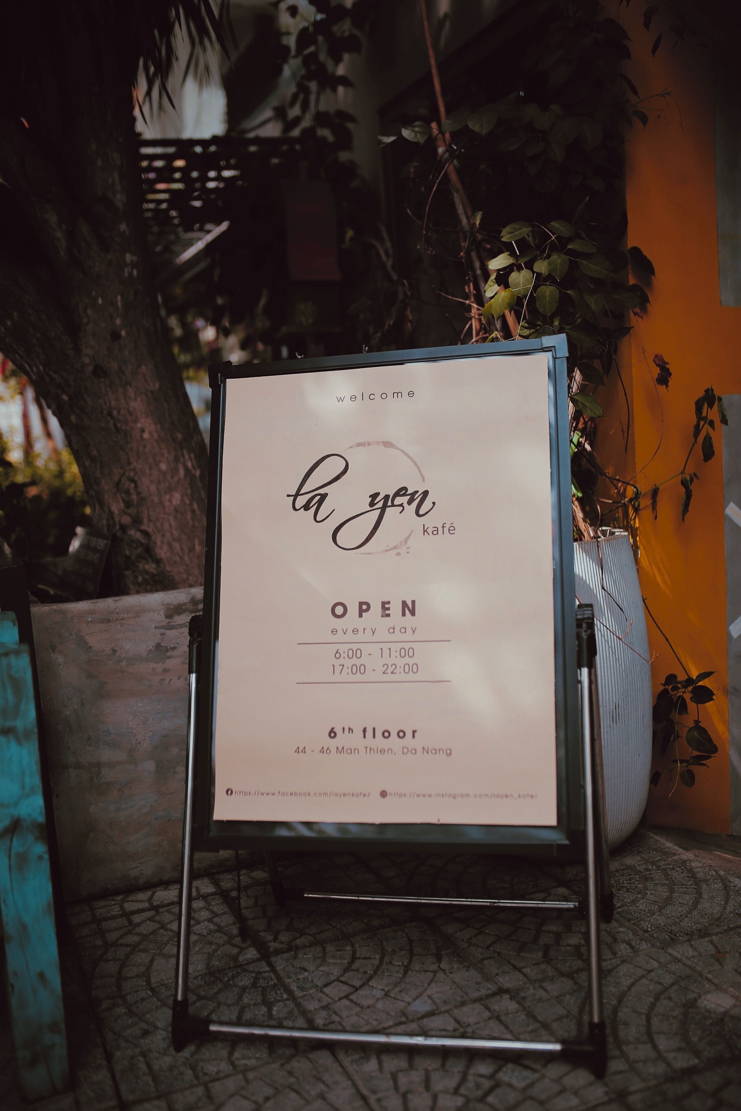 A signboard for 'la yen kafé' indicating it is open every day from 6:00 to 22:00, located on the 6th floor, 44-46 Mon Thien, Da Nang.