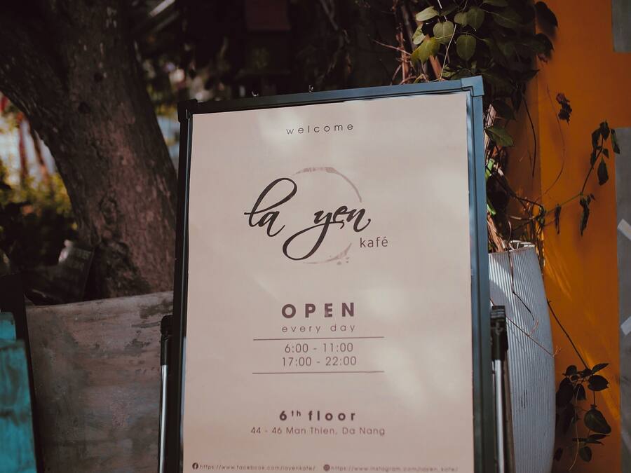 A signboard for 'la yen kafé' indicating it is open every day from 6:00 to 22:00, located on the 6th floor, 44-46 Mon Thien, Da Nang.