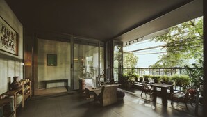 A spacious indoor area with a large glass door leading to an outdoor balcony, furnished with tables and chairs, and decorated with potted plants. - La Maison Des Delices (Da Nang)