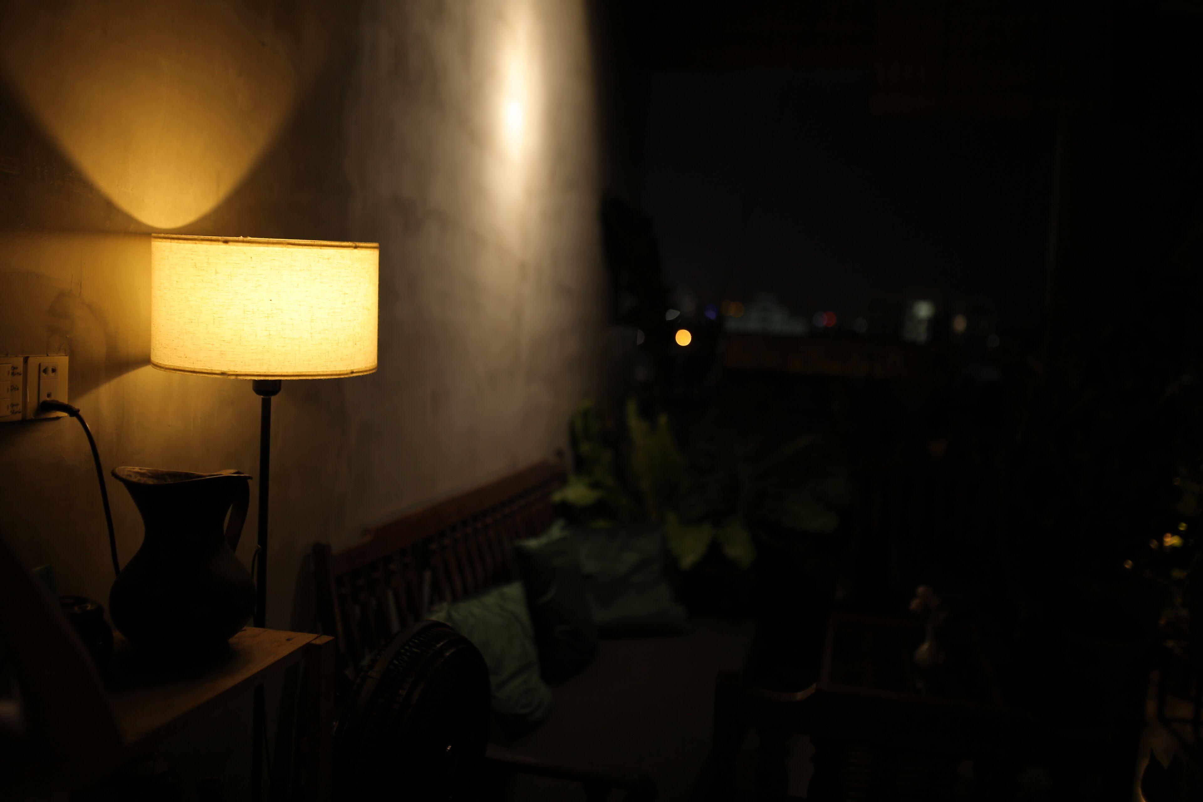 Une pièce faiblement éclairée, avec une lampe sur une table, un vase et un banc.