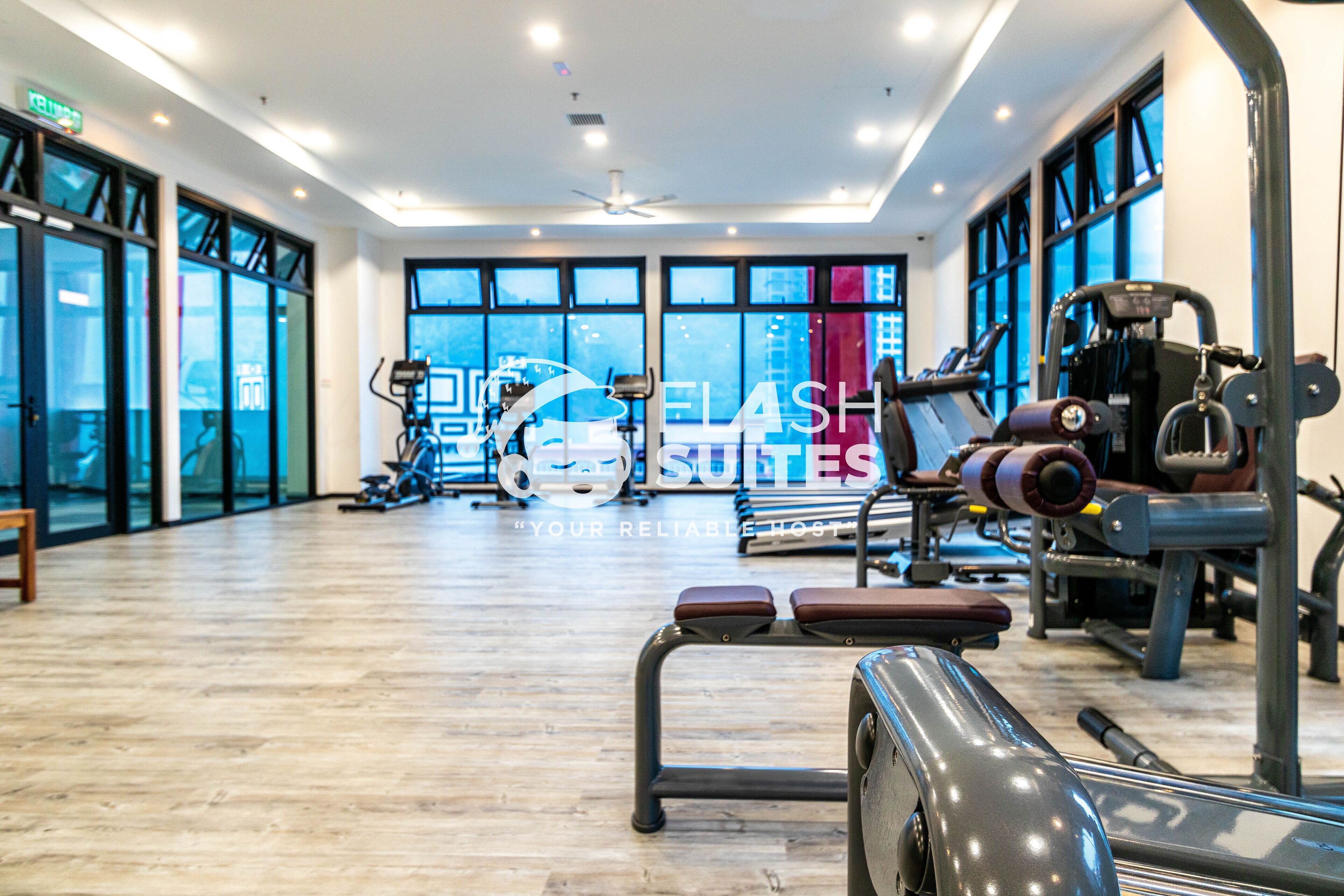 A gym with exercise equipment, large windows, and a wooden floor.