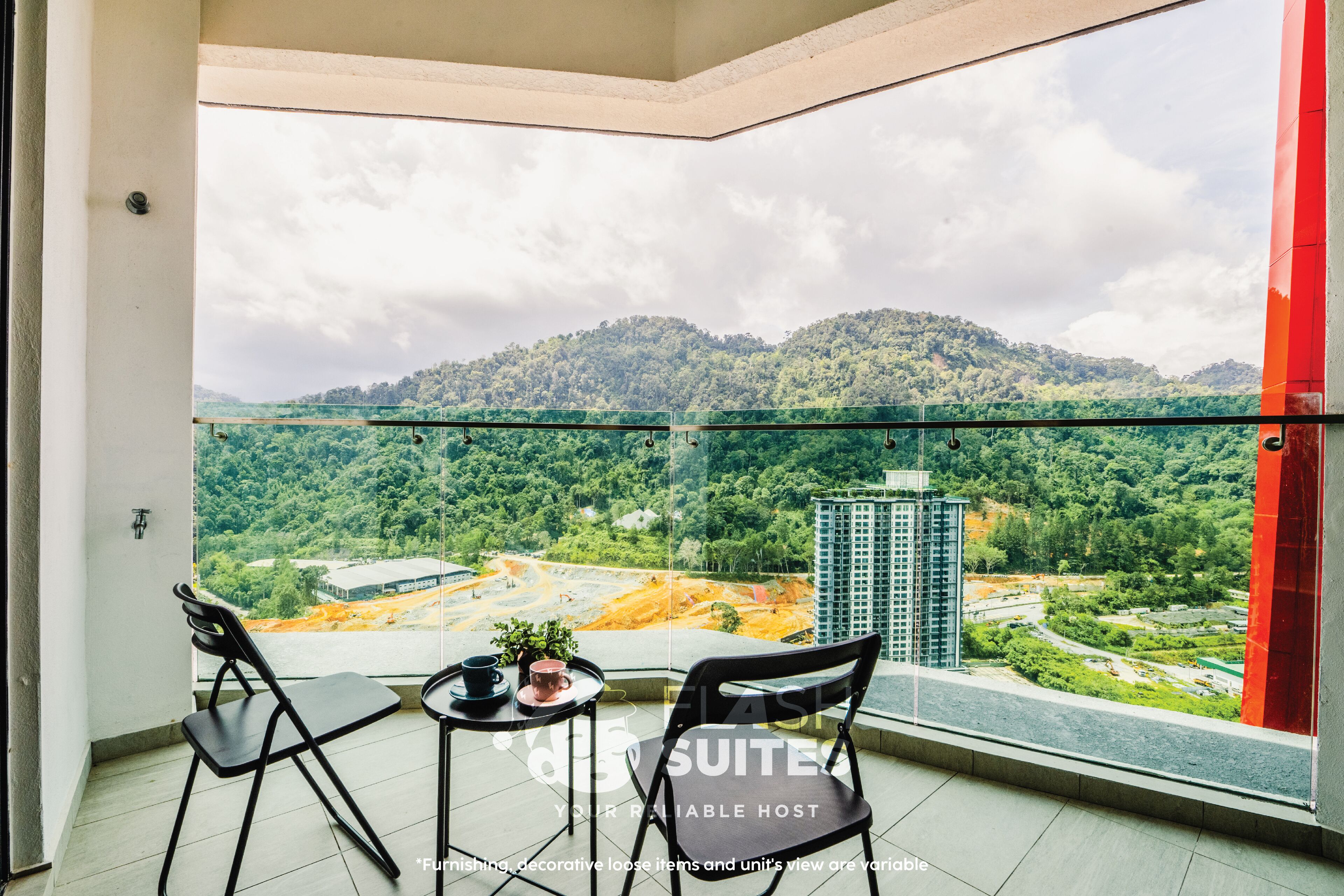 A balcony with two chairs and a small table, overlooking a construction site and a green hill.