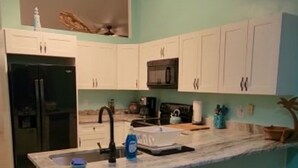 Una cucina con mobili bianchi, un frigorifero nero, un forno a microonde e un lavello.