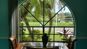 Zona pranzo con tavolo e sedie in vetro, un'ampia finestra ad arco che si affaccia su un giardino e una strada.