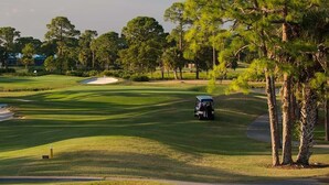 Un campo da golf con bunker di sabbia, un golf cart e cielo sereno.