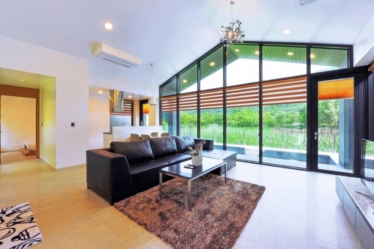 A modern living room with a black sofa, a coffee table, and a large window offering a view of greenery.
