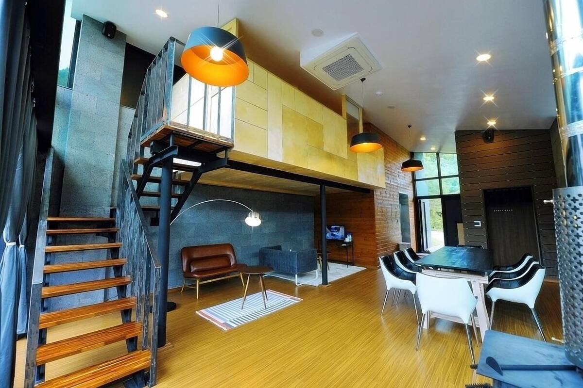 A modern interior with a wooden staircase, a dining area with white chairs, and a loft space with a view.