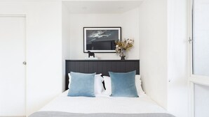 Quarto com cama, cabeceira escura, obra de arte emoldurada acima da cama e um vaso com flores na mesa de cabeceira.