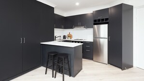 Uma cozinha moderna com armários escuros, geladeira de aço inoxidável, uma ilha central com banquetas e bancada branca.