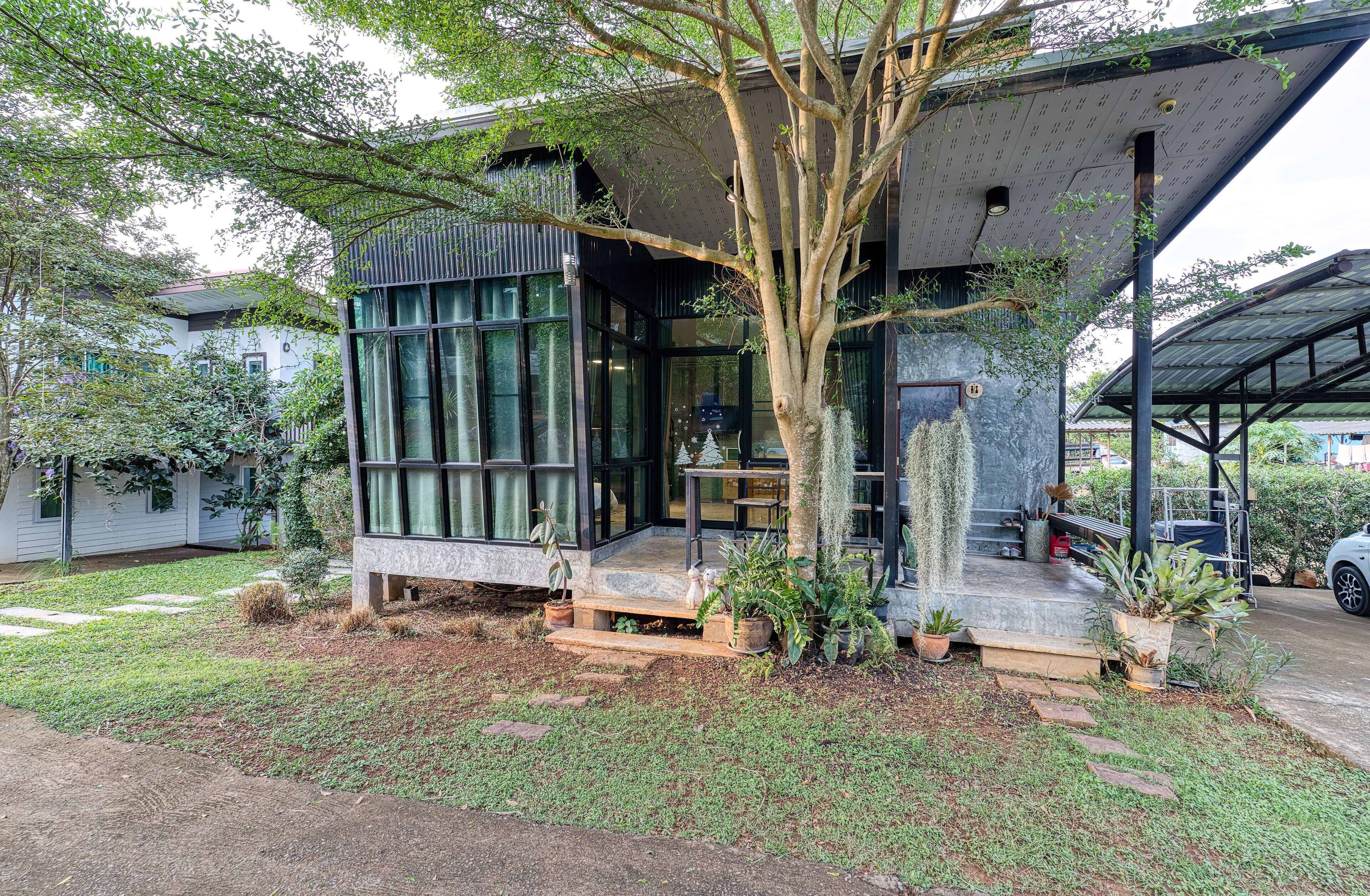 A modern house with a large glass window, a tree in front, and a car parked nearby.