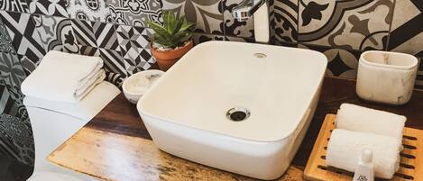 A bathroom with a white sink, a potted plant, a toilet, and a wooden counter with towels.