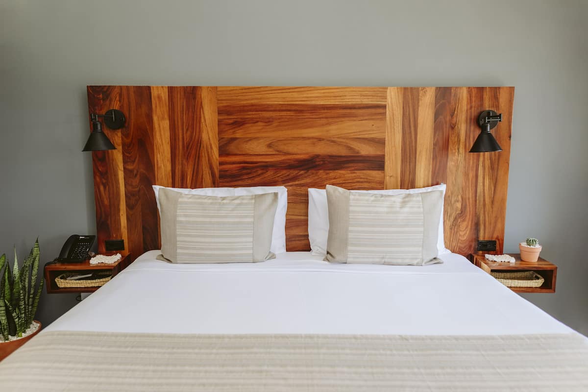 A bed with a wooden headboard, two bedside tables with lamps, a potted plant, and a telephone on one of the tables.