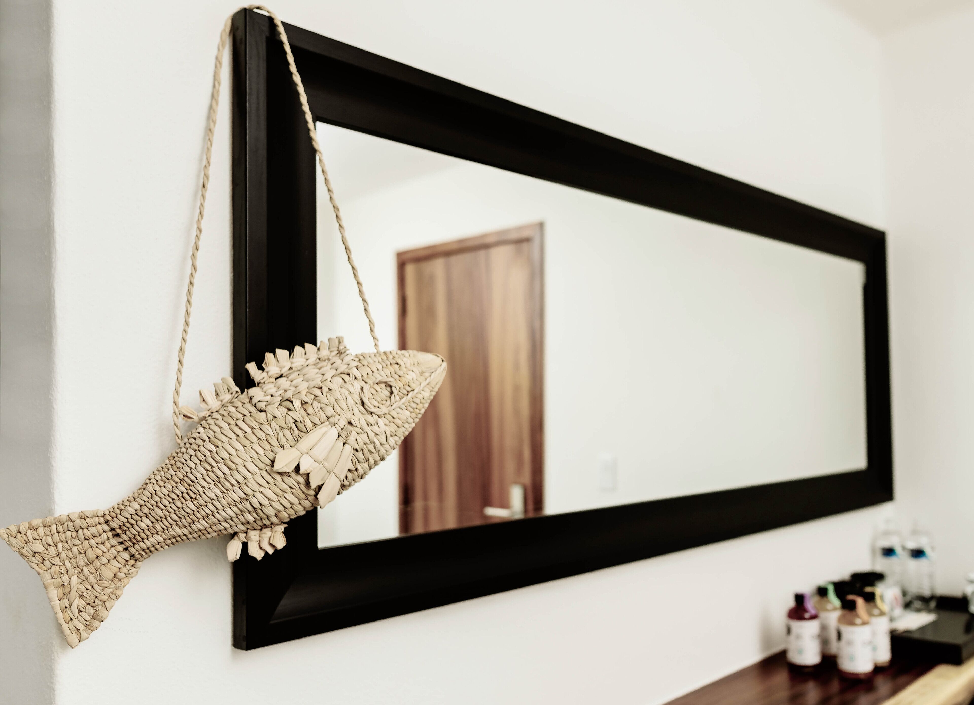 Un miroir encadré orné d’une décoration en forme de poisson tressé, accroché à un mur blanc.