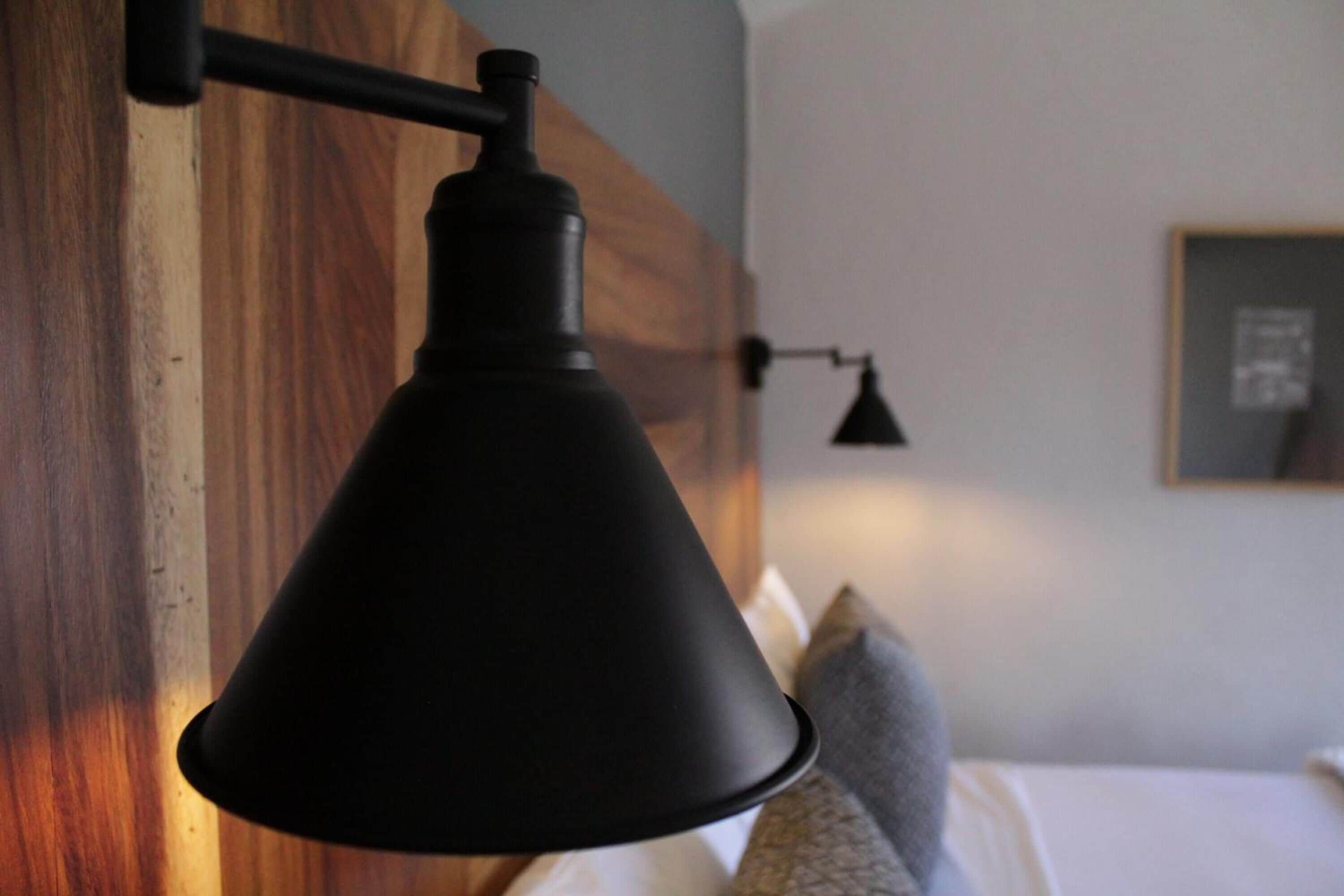 A black pendant lamp hanging from a wooden wall in a hotel room.