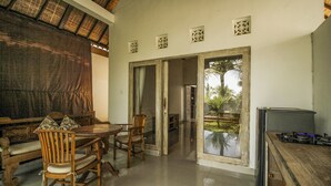 A dining area with a wooden table and chairs, a refrigerator, and a view of a garden through a glass door. - Villa Di Sawah Pejeng (Ubud)
