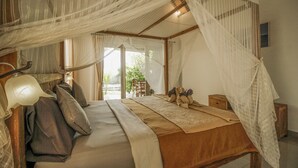A bedroom with a canopy bed, a bedside lamp, and a view of the outdoors. - Villa Di Sawah Pejeng (Ubud)
