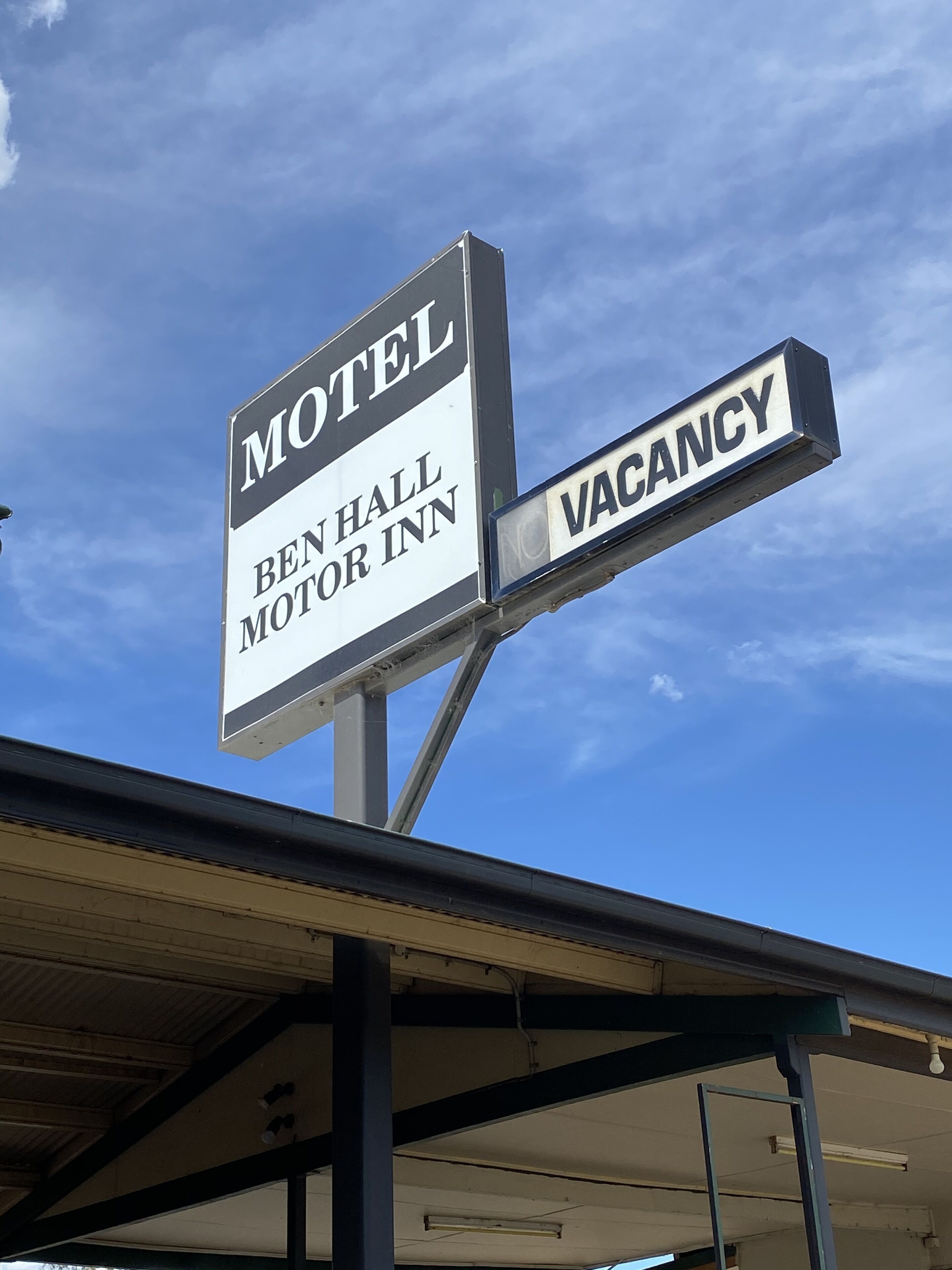 Letrero de motel que dice "BEN HALL MOTOR INN" y "HABITACIONES DISPONIBLES".