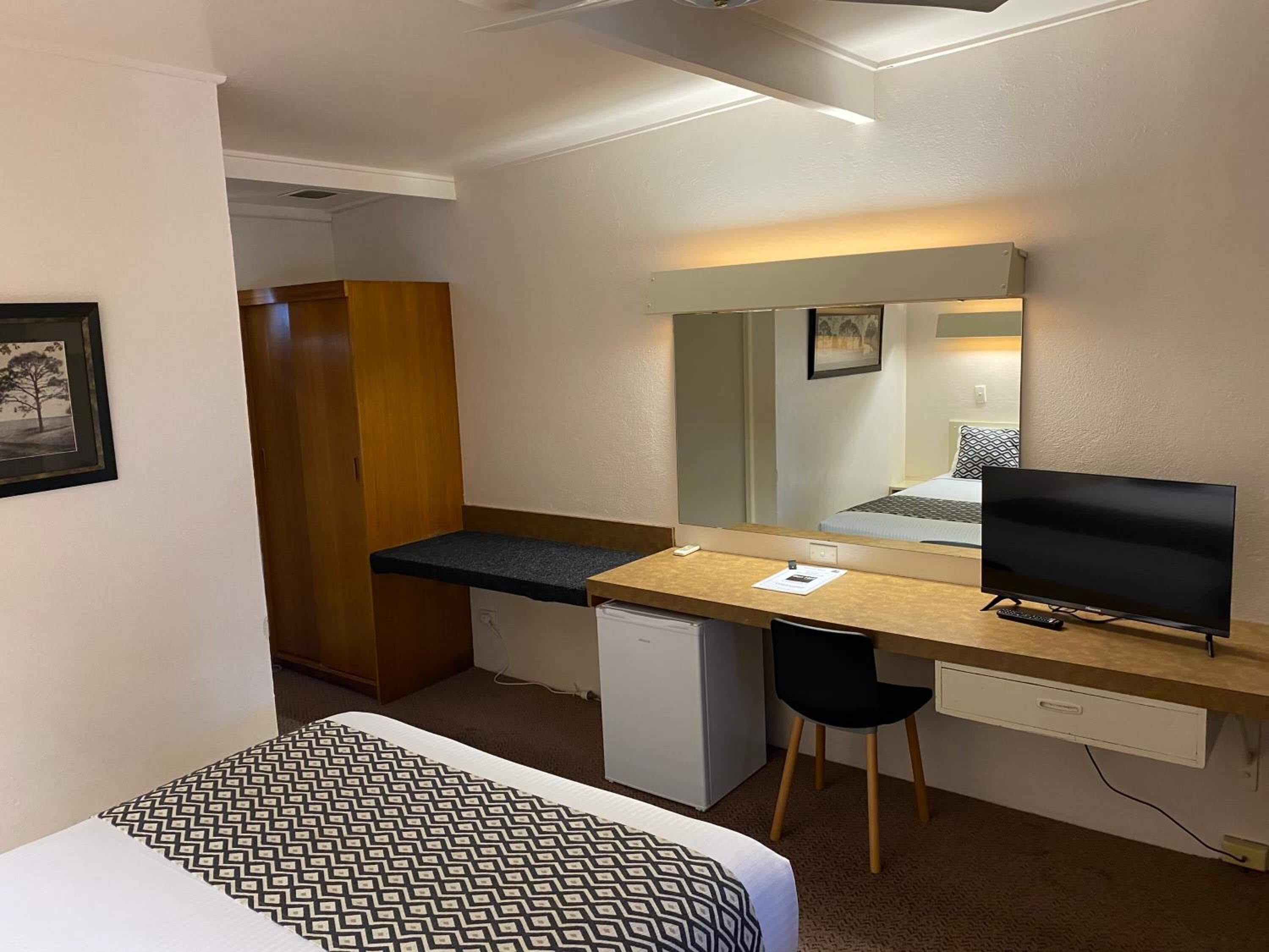 A hotel room with a bed, a desk with a computer, a television, and a wardrobe.