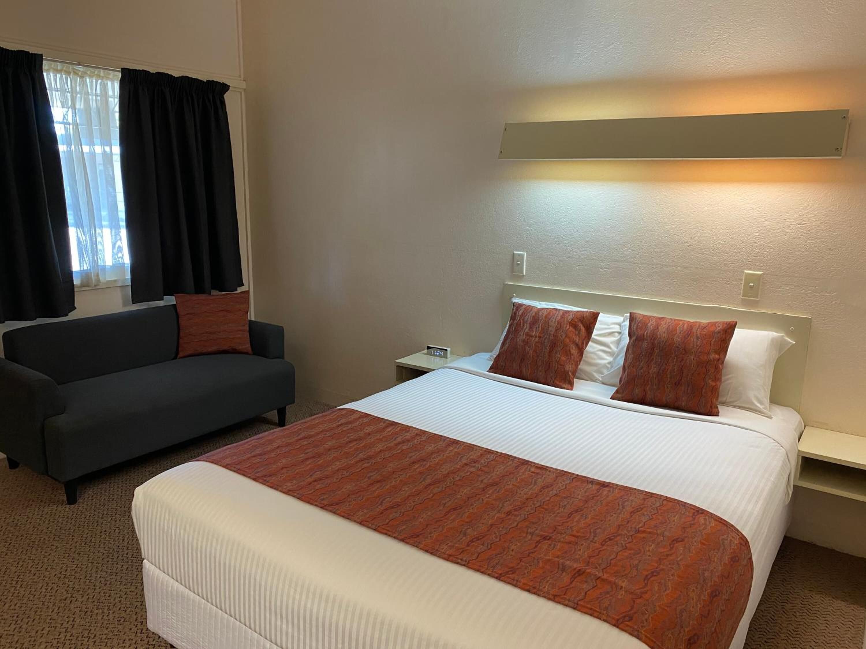 Habitación de hotel con una cama grande, un sofá, una mesita de noche y una ventana con cortinas.