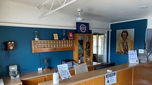 A reception area with a wooden counter, a hand sanitizer station, a blue wall with a 'BEN HALL' sign, a 'NOTICE' sign, and a ceiling fan.