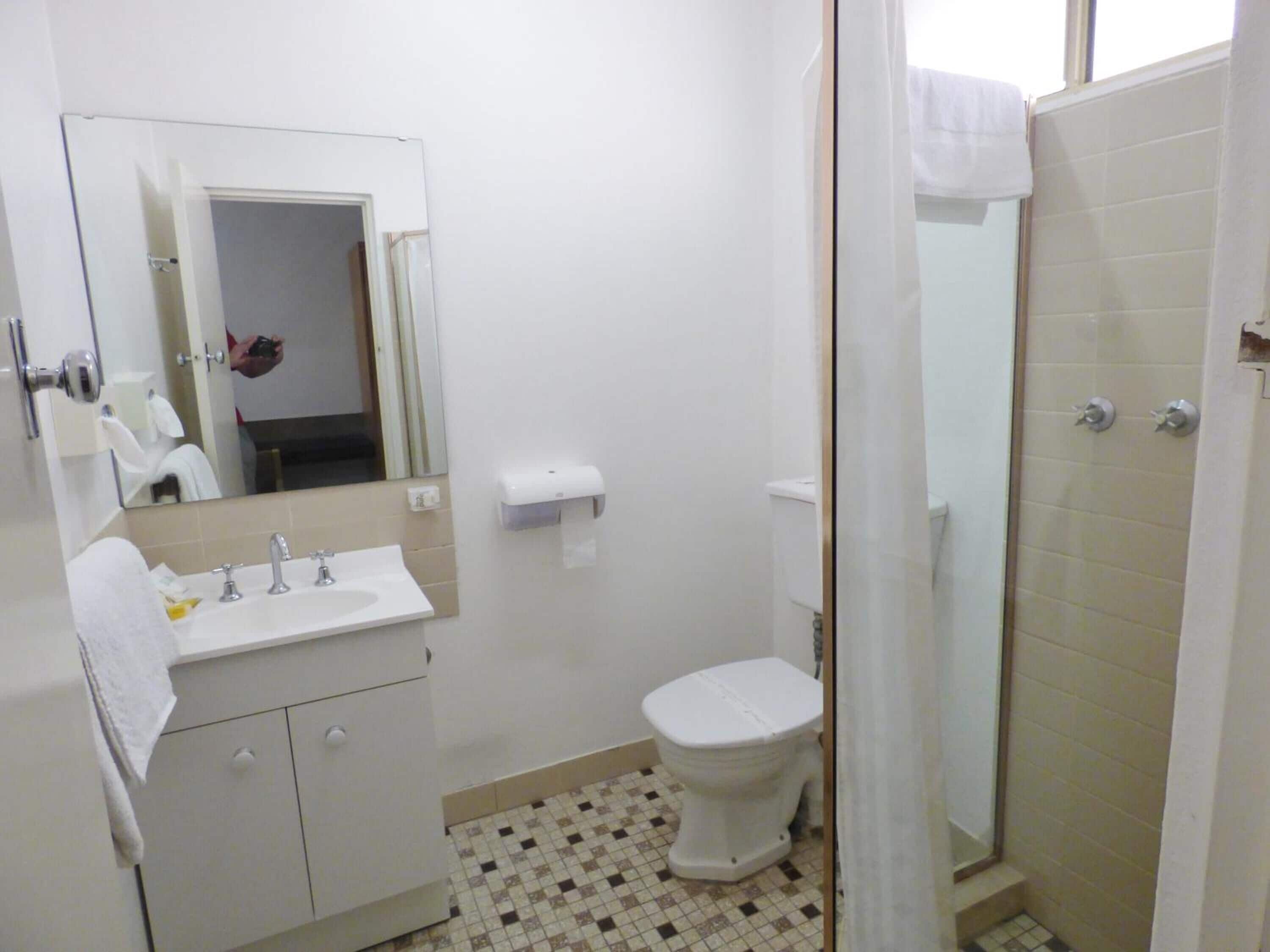 A bathroom with a sink, mirror, toilet, and shower area.