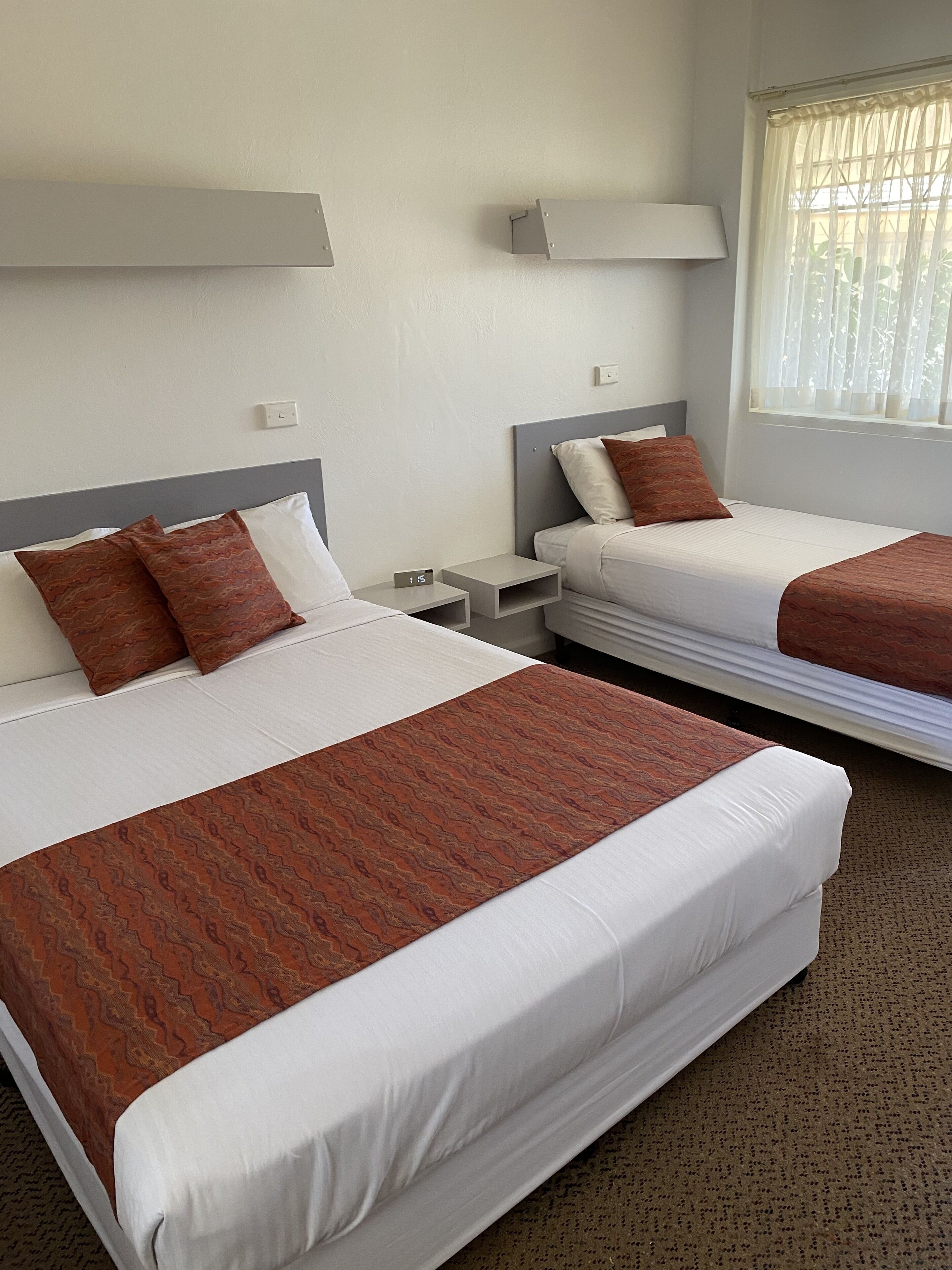 Habitación de hotel con dos camas, cada una con ropa de cama blanca y cabeceros marrones. Mesitas de noche con lámparas y un enchufe.