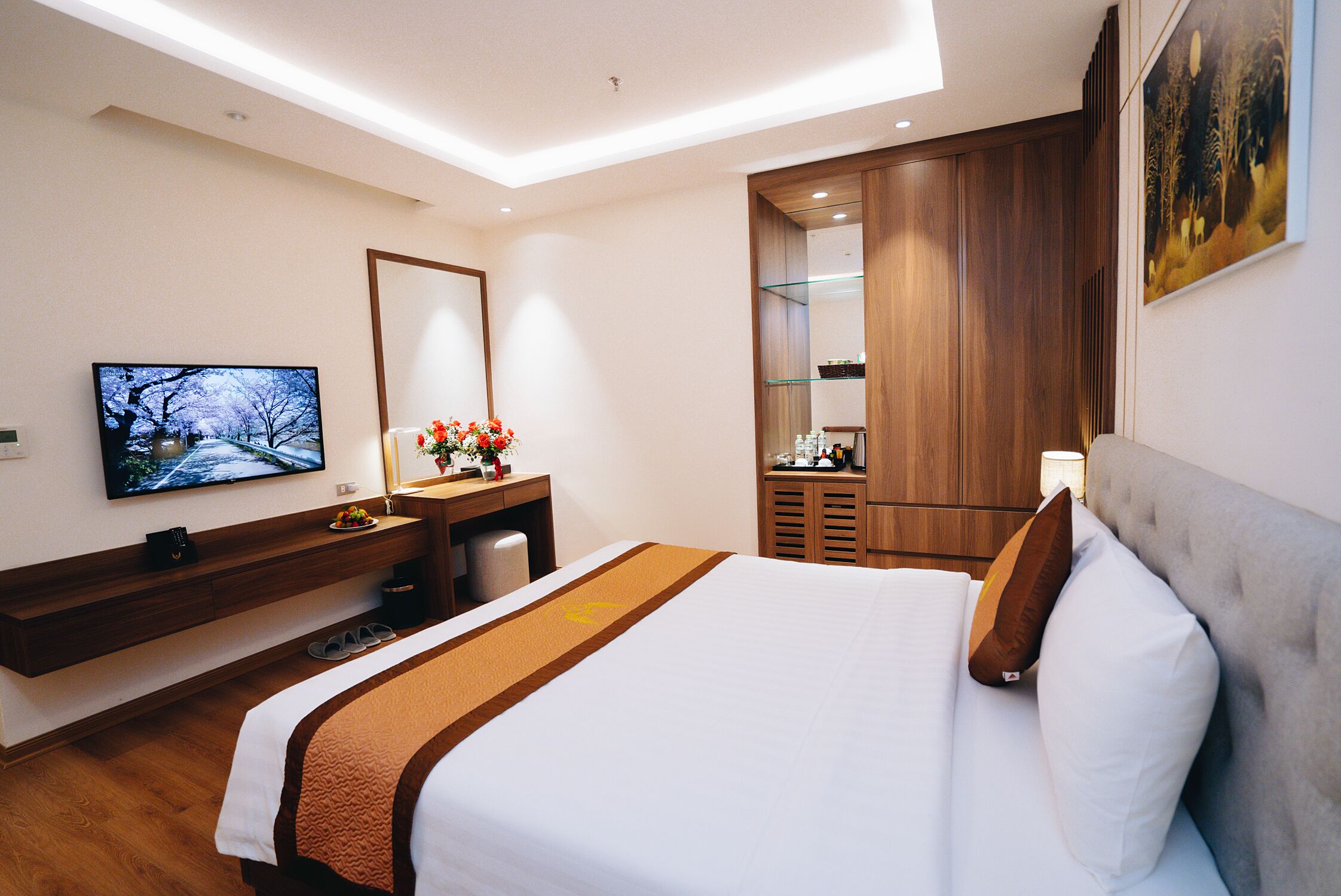 A modern hotel room with a large bed, a TV, a desk with a mirror, and a wardrobe.