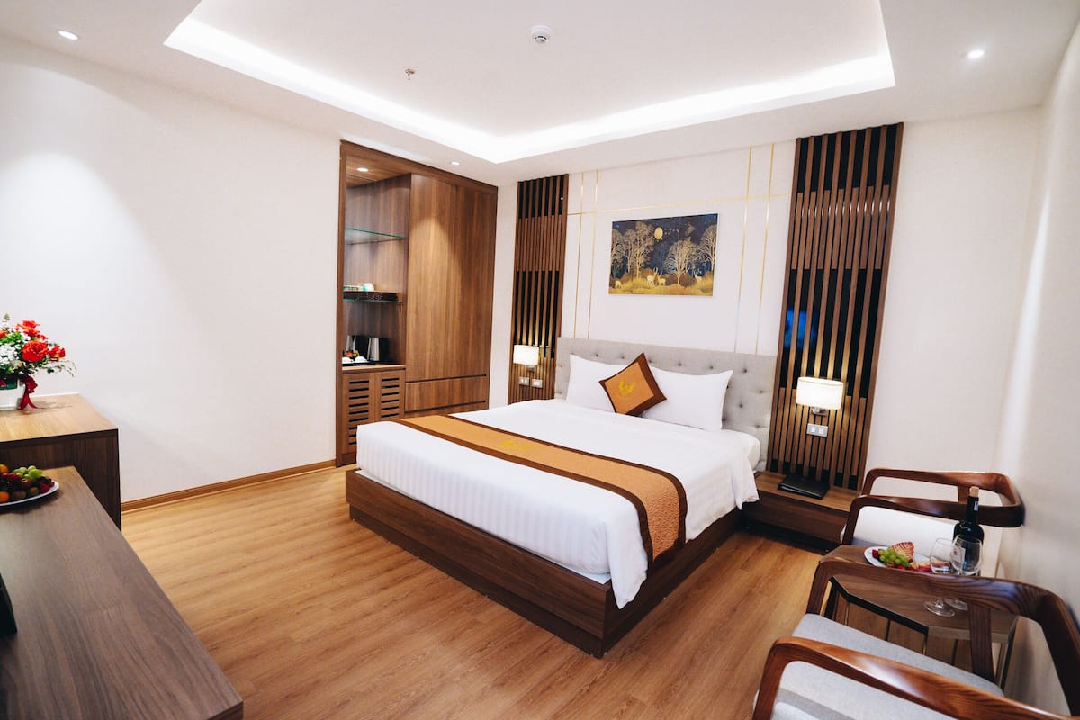 Una habitación de hotel moderna con una cama grande, muebles de madera, una zona de comedor y un cuadro en la pared.