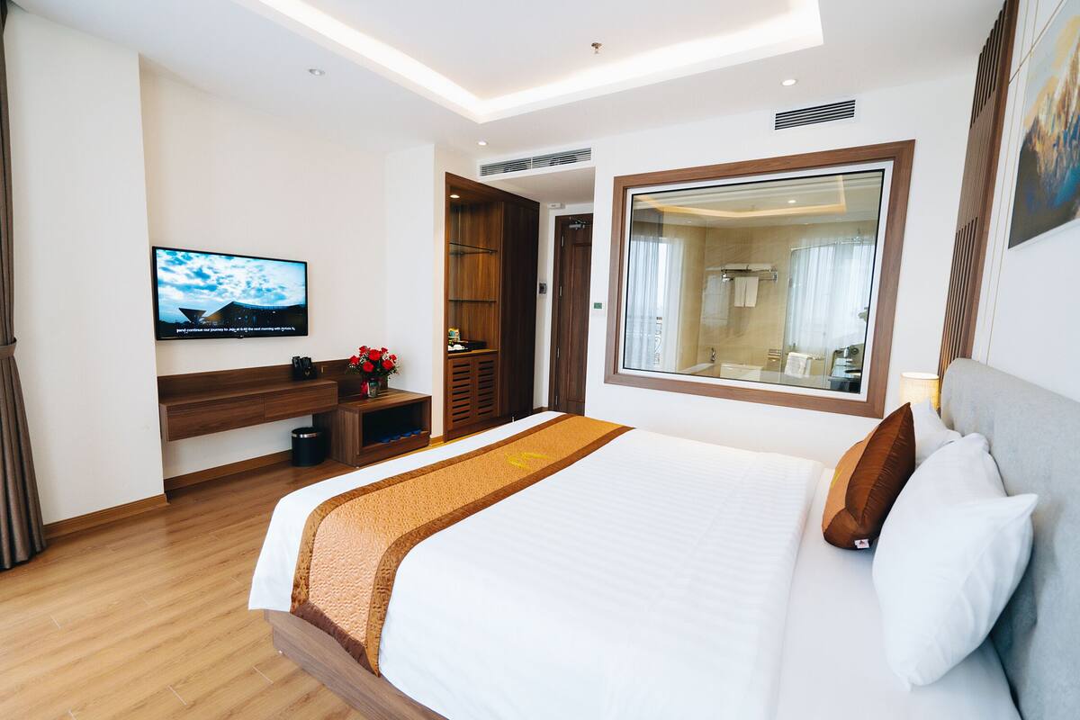 Una habitación de hotel moderna con una cama grande, un televisor montado en la pared, un escritorio de madera y un espejo sobre la cama.