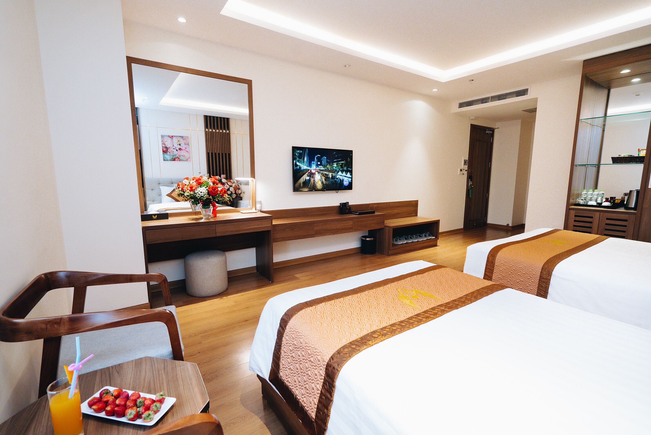 A hotel room with two beds, a TV, a desk with a flower arrangement, and a breakfast tray.