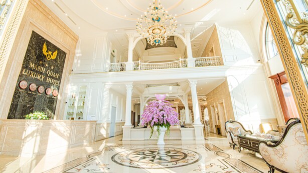 Een statige lobby met een kroonluchter, een bloemstuk en een bord met de tekst Man of Luxury Hotel.