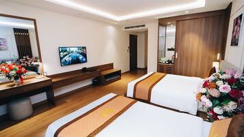 A hotel room with two beds, a TV, a desk with a vase of flowers, and a wooden wardrobe.
