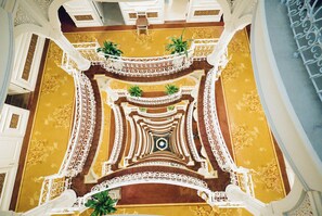 Un amplio atrio con barandillas blancas ornamentadas, una columna central y plantas en macetas.