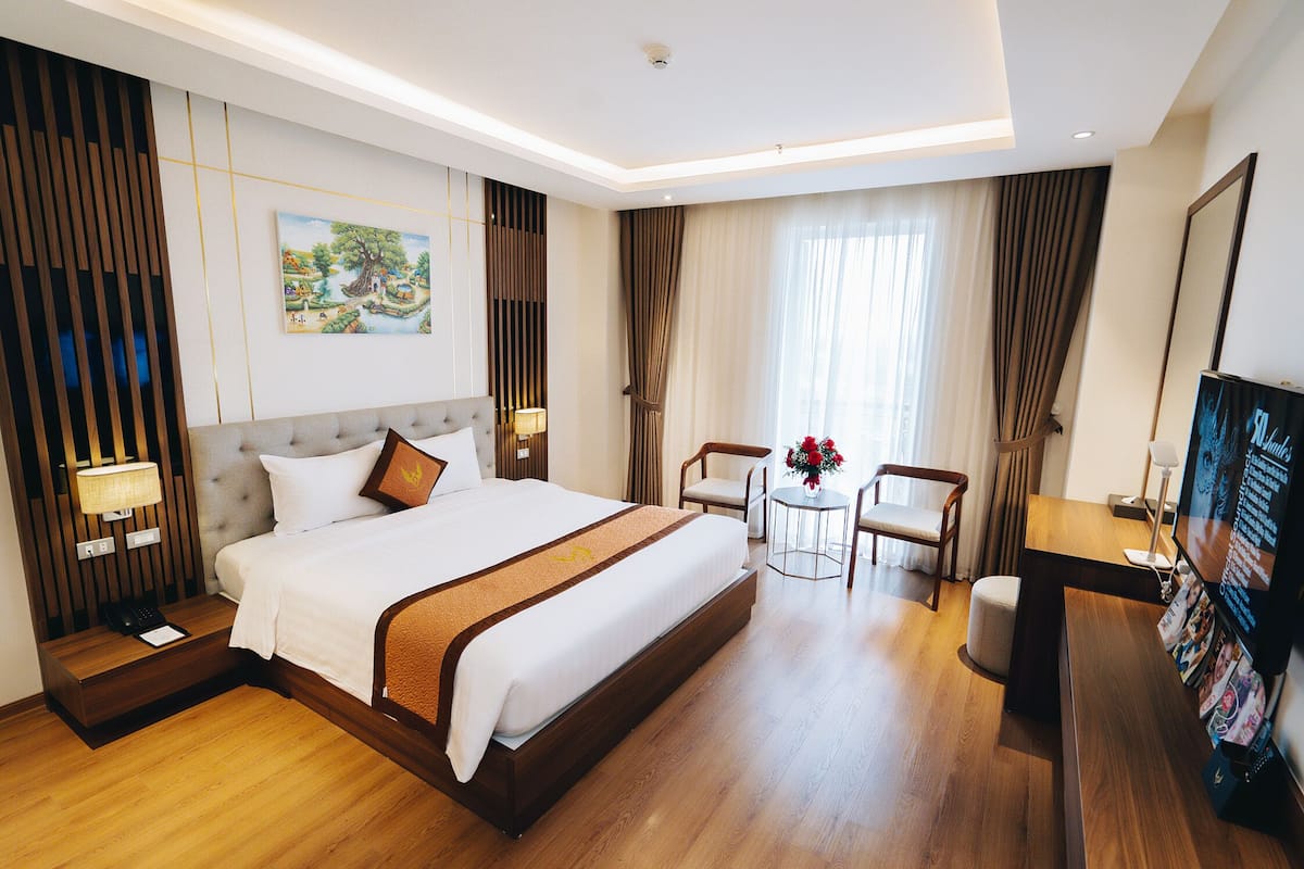 Habitación de hotel con una cama grande, un escritorio, una silla, un televisor y un cuadro en la pared.