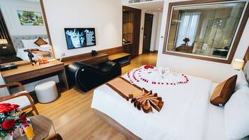 A hotel room with a bed, a desk, a chair, a TV, and a bathroom visible through an open door.
