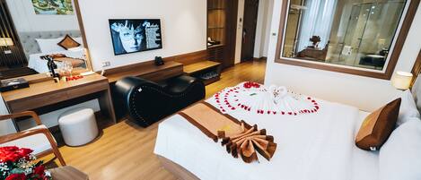 A hotel room with a bed, a desk, a chair, a TV, and a bathroom visible through an open door.