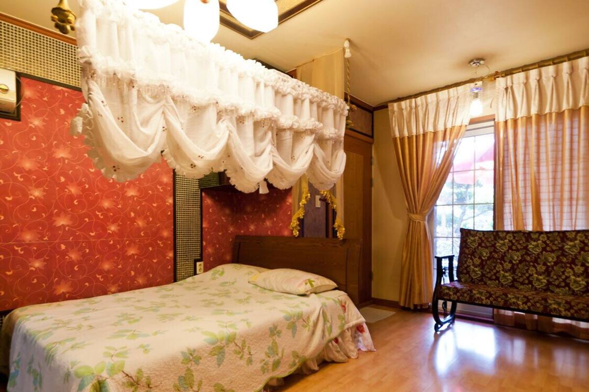 Une chambre à coucher avec un lit, un banc et une fenêtre avec des rideaux.