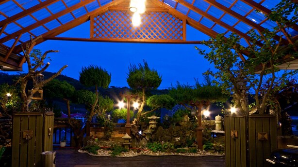 A covered outdoor area with a wooden pergola, stone lanterns, and various plants. - Taean White Sand Pension (Taean)