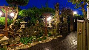 A nighttime garden with stone lanterns, a wooden pergola, and a wooden pathway. - Taean White Sand Pension (Taean)