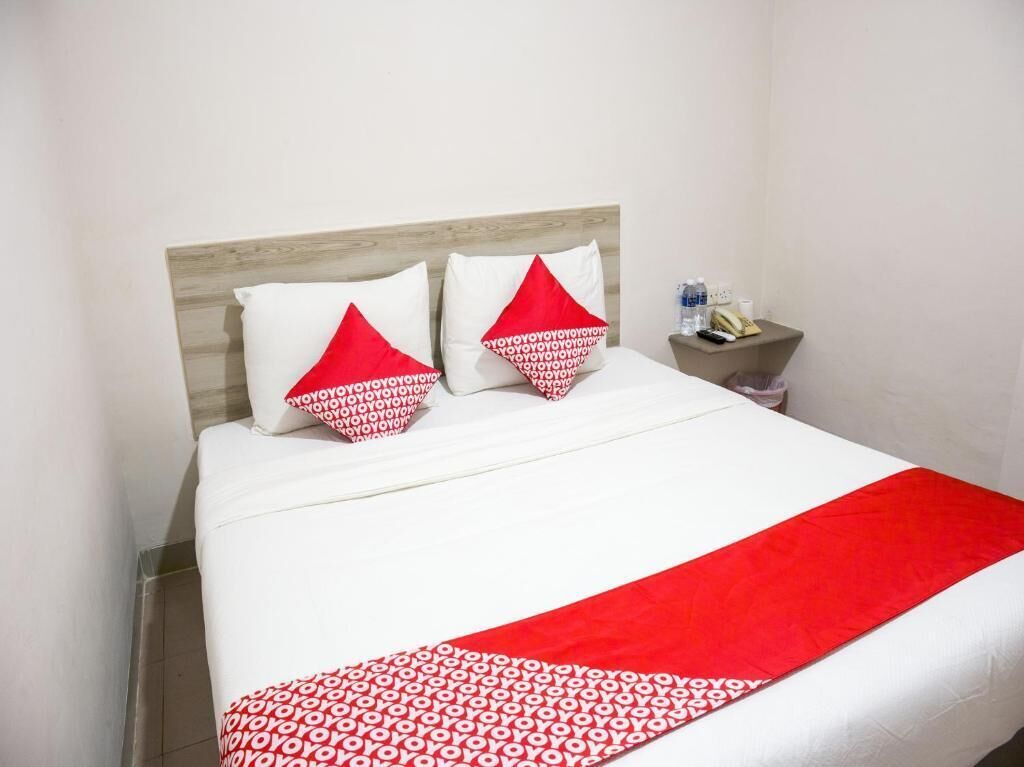 Un lit avec une literie blanche et une couverture rouge, deux oreillers à motifs rouges et blancs, et une tête de lit en bois.