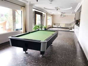 A pool table in a well-lit room with large windows, a staircase, and a sofa.