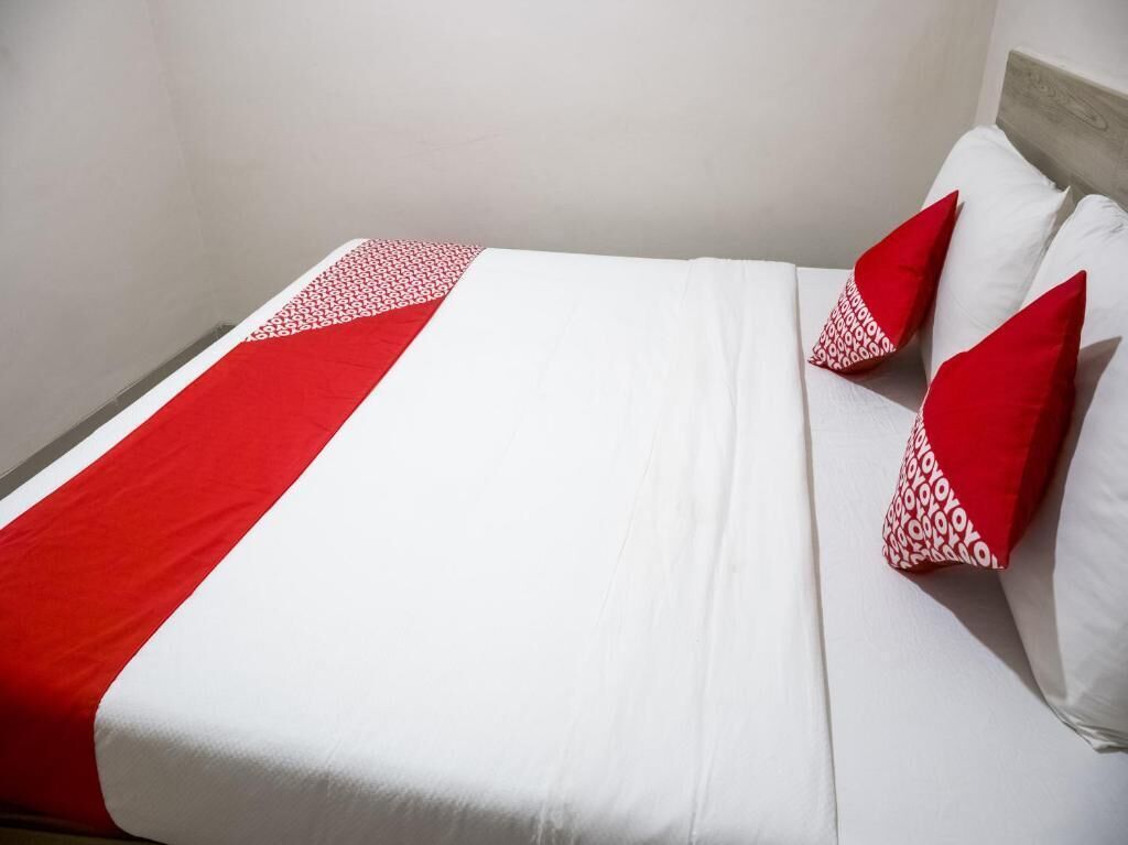 Ein Bett mit weißroter Bettdecke, zwei Kissen mit roten und weißen Mustern und einer schlichten Wand.