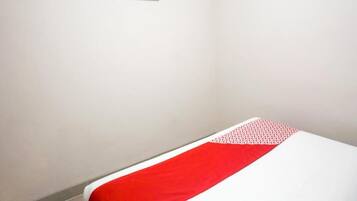 Una habitación con una cama, un pequeño televisor montado en la pared y una colcha de edredón con motivos rojos y blancos.